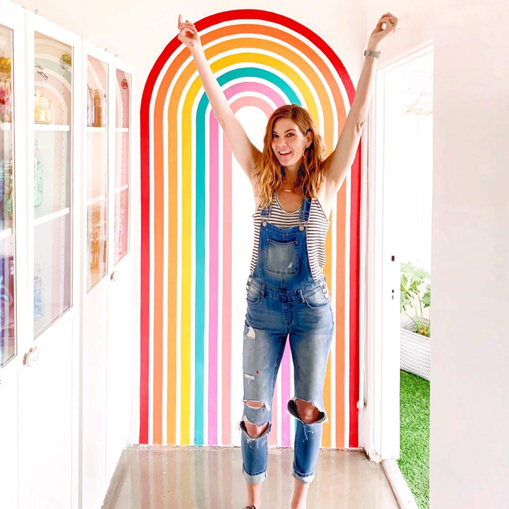 Stefanie Bales Fine Art poses in front of her rainbow mural.